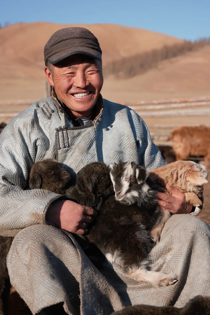 A Mongolian herder smiling with young goats in his arms