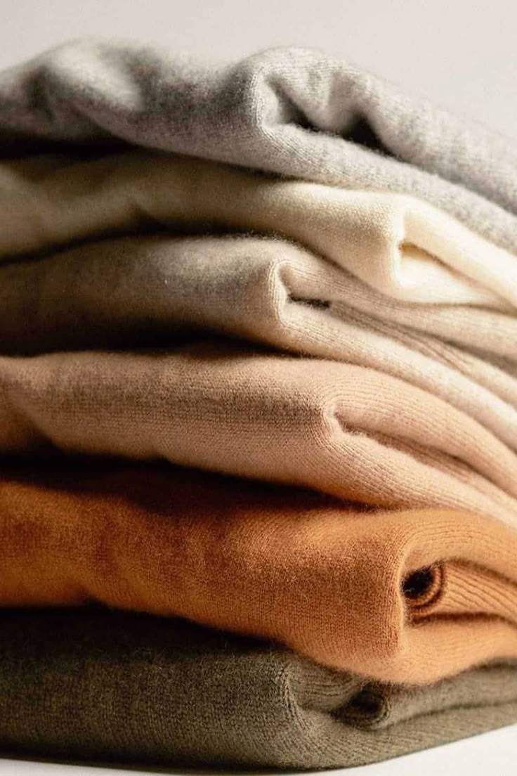 A stack of folded cashmere sweaters in natural tones
